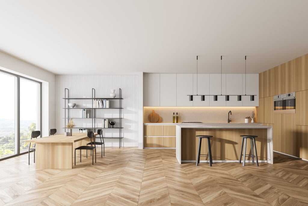 Modern kitchen with wooden cabinets, white countertops, and herringbone wood flooring. Features an island with barstools, a dining table with chairs, open shelves with decor, and large windows overlooking a scenic view.